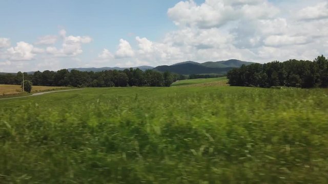 Driving past a rolling grassy plain with trees in the background and mountains on the horizon.