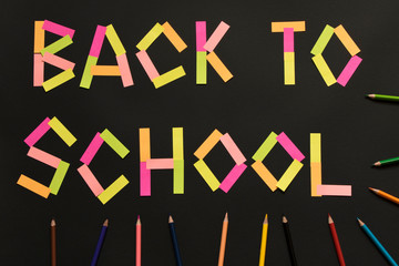 Inscription Back to school from colored stickers on the blackboard with colored pencils.