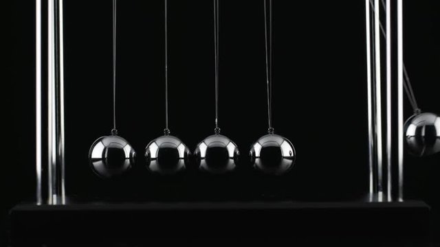 The chrome balls of a Newton&rsquo;s Cradle colliding in slow motion