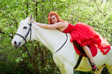 Girl in beautiful red dress on white horse in Park or forest. Photo shoot models and fashion