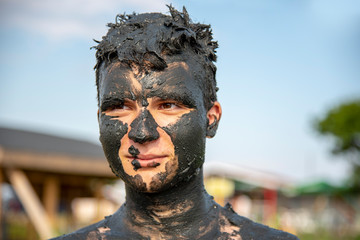 Teenager smeared with mud, visible minor patches of skin.
