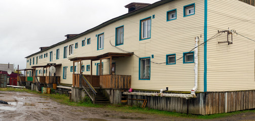 Apartment building in the Northern village of Yakutia Suntar with a floor above the ground made of wood sheathed siding next to the dirty road and puddles.