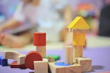 baby playing analogue colorful wooden toy. creative play for children brain development. image focus on toys and baby sitting out of focus in the background.