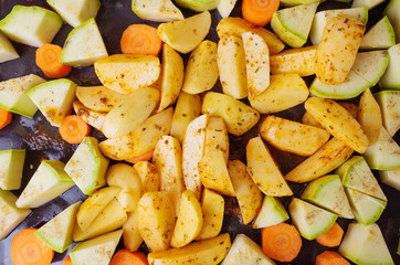 Vegetables - zucchini, potatoes and carrots - lie on a baking sheet, sprinkled with spices. The concept of cooking vegetarian food, a fresh crop of vegetables, a healthy diet.