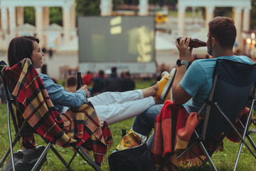 couple sitting in camp-chairs in city park looking movie outdoors at open air cinema