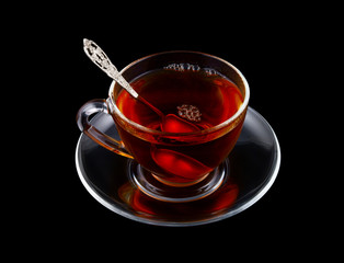Glass cup of tea with spoon isolated on black background