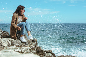 woman sitting on cliff enjoying view of the sea. windy weather. sunny day