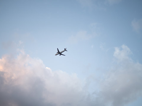 Flying plane in the sky with clouds at sunset as a background
