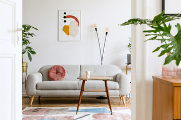 Stylish retro and vintage interior of sitting room with design sofa, table, bookstand and mock up poster frame on the white walls. Interior design with brown wooden parquet and plants.