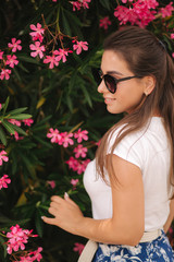 Gorgeous woman in sunglasses stand in beautiful flowers. Portrait of happy smiled young woman