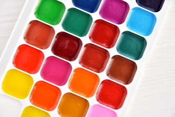 Bright multicolored aquarelle paints in paint box with selective focus on neutral background. Vivid watercolor paint. Palette with new bright watercolors for drawing. Back to school. Set for artist. 
