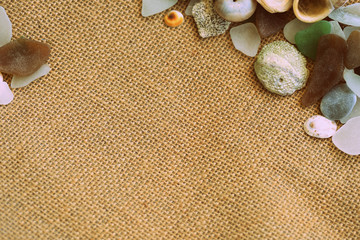 Shells, sea glasses and stones on a jute background close-up brown color toned. Vacation concept