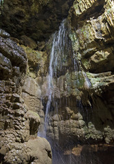 Fototapeta na wymiar Geological rock formations and waterfall in an underground cave