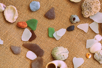 Shells, sea glasses and stones on a jute background close-up brown color toned. Vacation concept