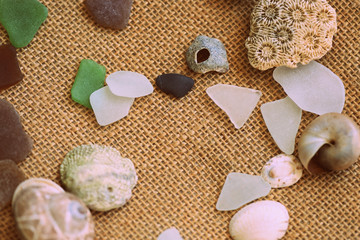 Shells, sea glasses and stones on a jute background close-up brown color toned. Vacation concept