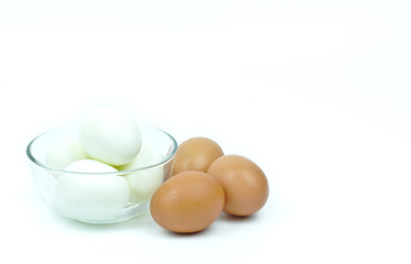 Isolated of four hard boiled chicken eggs in clear glass bowl and three raw eggs on white background with copy space on the right and upper.