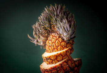 Close up of a sliced pineapple with crazy hair style top against a dark green blurred background