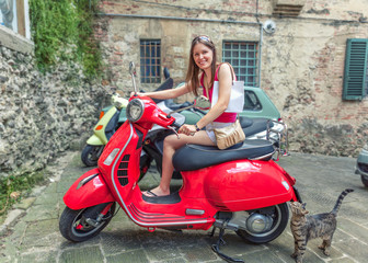 Plakat Young beautiful girl rides a red motor scooter Vespa through the streets of Rome, Italy.