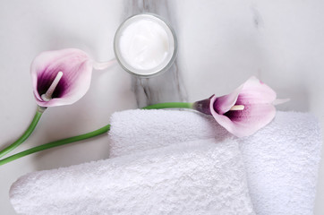 Purple callas, moisturizing cream, fresh white towels on the white surface
