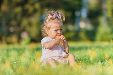 Cute little girl sits on the green grass, outdoors, summer time, blurred background
