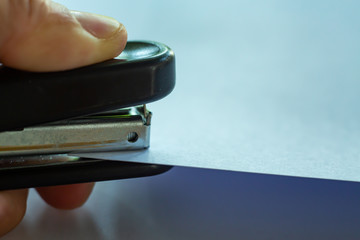 Woman's left hand holding stapler and stapling white paper on grey colour background, Close up &...