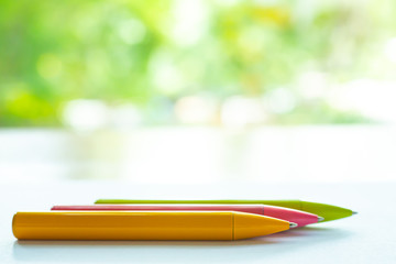 Blurred 3 colour pens ( Yellow, Pink, Green ) on white paper, Bokeh green garden background, Notebook, Close up & Macro shot, Selective focus, Communication, Stationery concept
