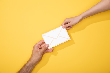 cropped view of man and woman holding paper icon of white envelope on yellow