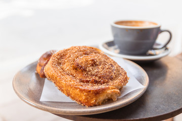 Warm cinnamon bun with icing sugar with a cup of coffee lying on the table in a street cafe.