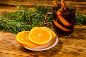 Cup of mulled wine with cinnamon, sliced orange and fir tree branches on wooden table