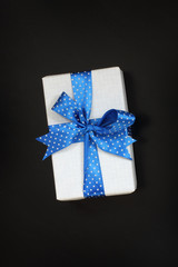 gift with a blue ribbon with polka dots on a dark background top view. surprise for the holiday