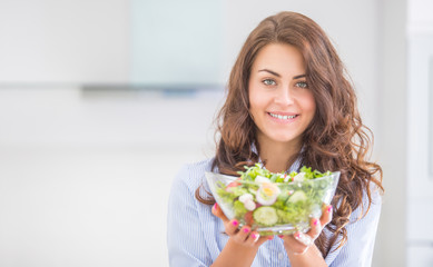 Young woman holding bowl with salad in her kitchen. Healthy lifestyle concept beautiful woman with...