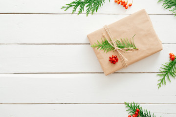 Christmas minimal composition. Xmas present wrapped kraft paper and fir tree branches on wooden white background. New year, Christmas concept. Flat lay, top view, copy space.