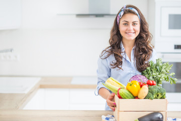 Woman in her kitchen with wooden box full of organic vegetable