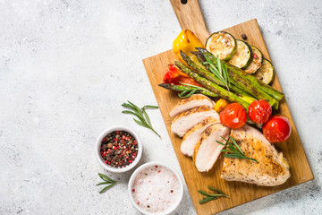 Chicken breast grilled with vegetables on a wooden serving board.