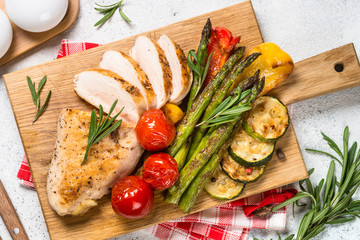 Chicken breast grilled with vegetables on a wooden serving board.