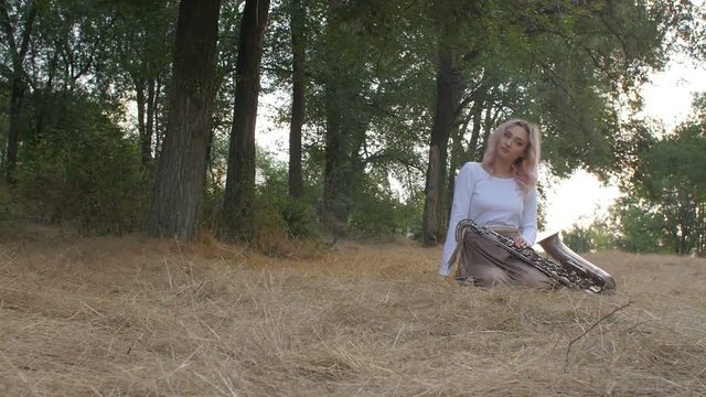 young beautiful romantic girl sitting on the ground on hay on the ground with a saxophone, a woman with a musical instrument, concept hobby, music, lifestyle