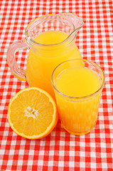Orange juice in glass and pitcher on red tablecloth