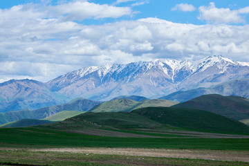 View of mountain snowy ridges on a bright sunny day with clouds in the sky.