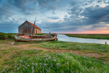 Summer sunrise over an old coal barn and fishing boat at Thornham on the north coast of Norfolk