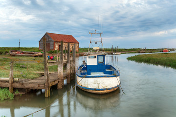 Fototapeta na wymiar A fishing boat moored at a wodden jetty at Thornham