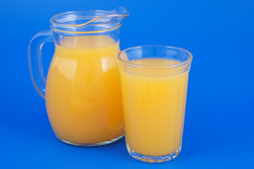Orange juice in glass and pitcher on blue background