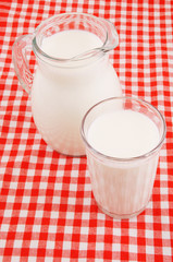 Milk in jar and glass on red checkered tablecloth