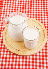 Milk in pitcher and glass with wooden board on red tablecloth 
