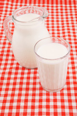 Milk in pitcher and glass on red tablecloth 