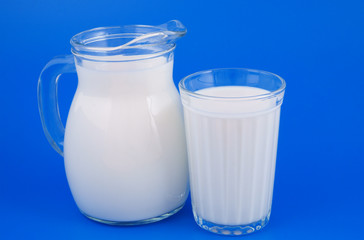 Pitcher and glass with fresh milk on blue background 