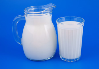 Glass and pitcher with milk on blue background 
