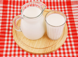 Milk in pitcher and glass with wooden board on red tablecloth