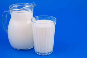 Glass and jar with milk on blue background with space for text