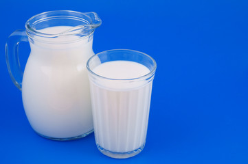 Glass and pitcher with milk on blue background with space for text