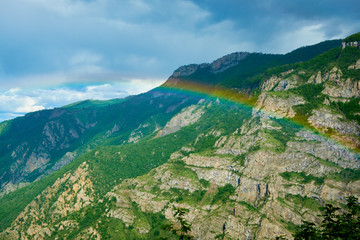 Fototapeta na wymiar Rainbow in the mountains after a rain on a sunny day with clouds in the sky.